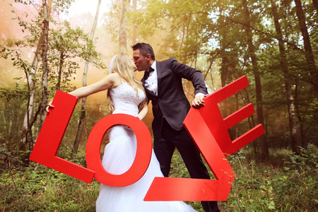 Bride and groom holding big LOVE letters in the forest, surrounded by red smokeの写真素材