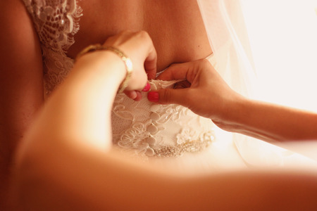 Hands of bridesmaid helping the bride with wedding dressの写真素材