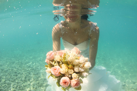 Hands of a bride holding wedding bouquet underwaterの写真素材