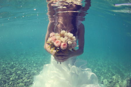 Hands of a bride holding wedding bouquet underwaterの写真素材