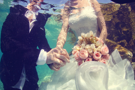 Bride and groom holding hands underwaterの写真素材