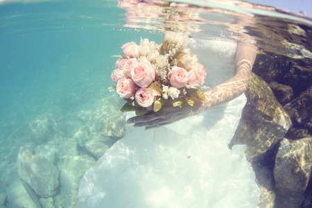Hands of a bride holding wedding bouquet underwaterの写真素材