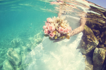 Hands of a bride holding wedding bouquet underwaterの写真素材