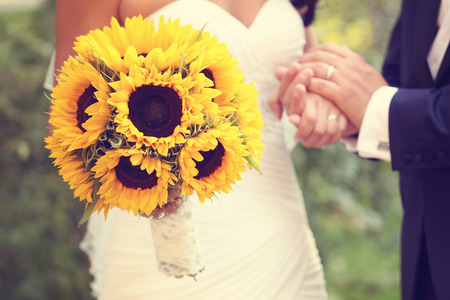 Hands of a bride and groom holding sunflower bouquetの写真素材