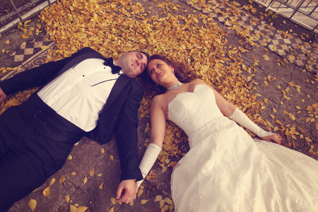 Bride and groom laying on autumn leavesの写真素材