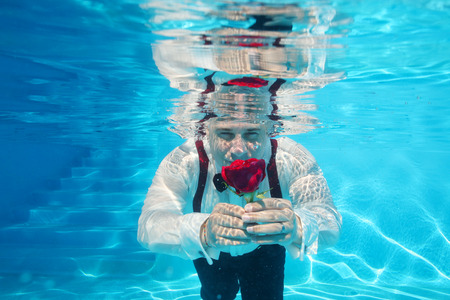 Handsome groom underwater diving giving a red rose flowerの写真素材