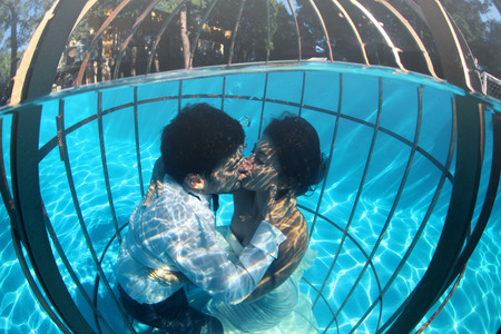 Romantic bride and groom underwater in a bird cage