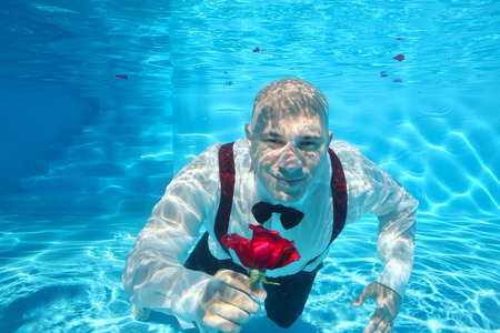Handsome groom underwater diving giving a red rose flowerの写真素材
