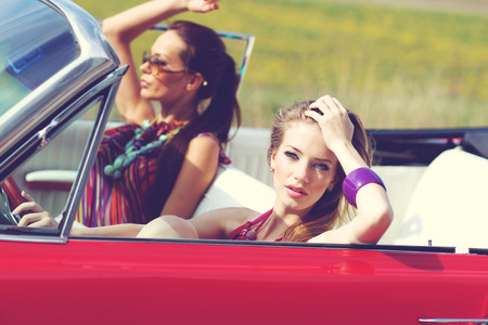 Beautiful ladies with sun glasses riding a vintage retro carの写真素材