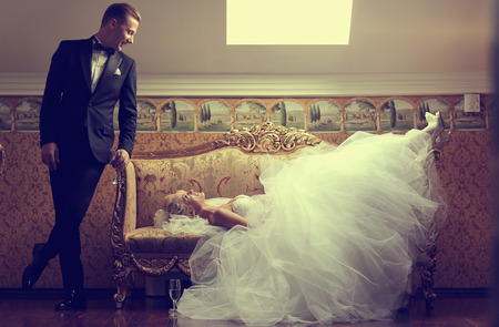 Beautiful bride on a sofa and groom near her in a luxury hotelの写真素材