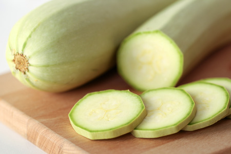 Green white zucchini sliced and whole with knife on wooden cutting boardの写真素材