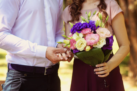 Beautiful bridal couple embracing in park and holding bouquetの写真素材