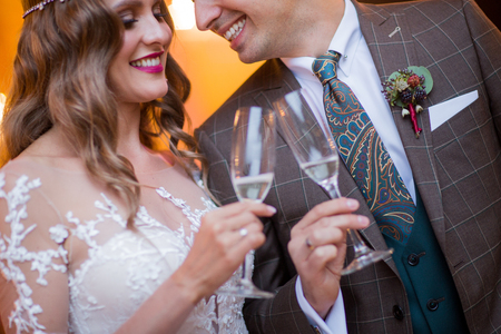 glass of wine in hands of beautiful bride and handsome groomの写真素材