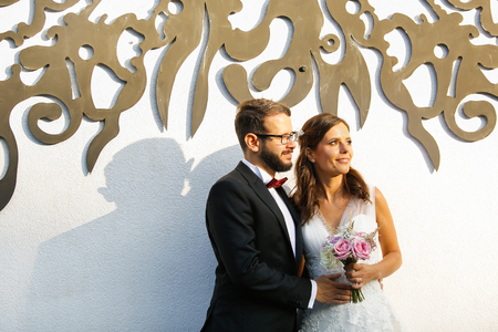 Beautiful wedding couple posing in front of white wall on sunの写真素材