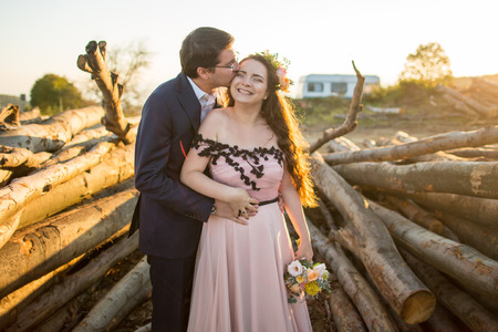 Beautiful young wedding couple, bride and groom posing near wooden cutの写真素材