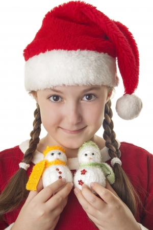 Beautiful girl dressed in Christmas clothes and red santa hat with two cute little snowmen in her hands isolated on white backgroundの写真素材