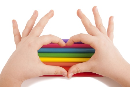 Child hands form a heart shape above color pencils isolated on whiteの写真素材