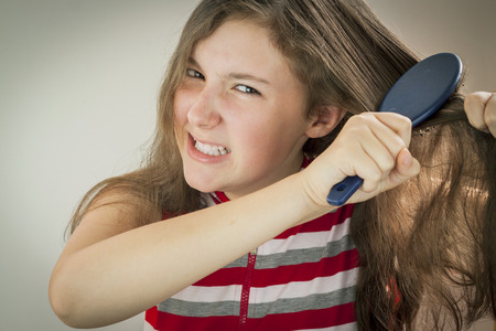 Dissatisfied with teen girl combing her long hair tangledの写真素材