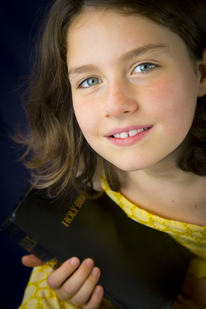 Portrait of beautiful little girl holding Holy Bible. Closed bible