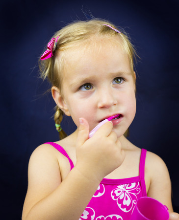 Beautiful little girl with blond hair holding spoon. Blue backgroundの写真素材