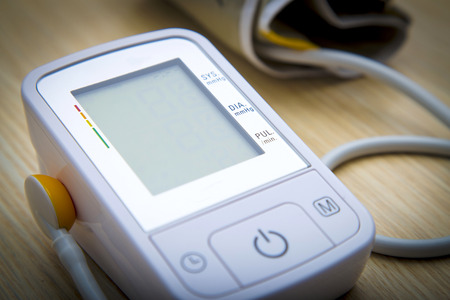 Digital blood pressure meter on wooden table with blank monitorの写真素材
