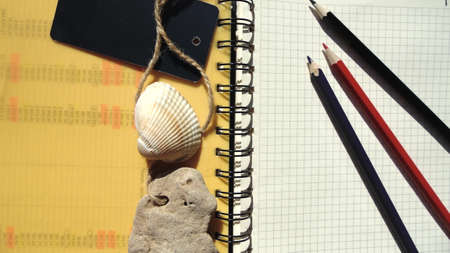 A notebook with yellow and white pages, three colored pencils, and a seashell stone. Office,...