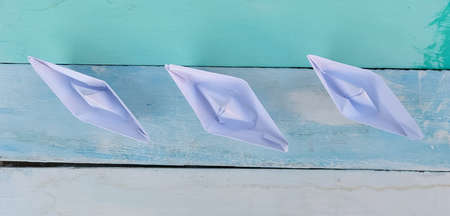 Three white paper boats on a wooden background painted in blue.