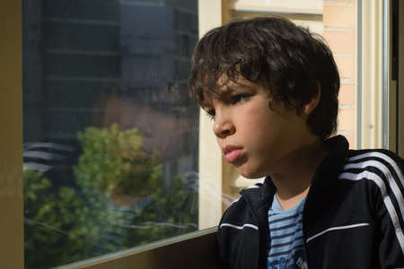 a sad boy looking out through a window