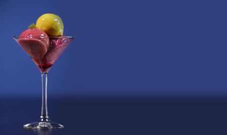 Yellow and red ice cream balls in a glass canister. Isolated against a blue background.Panorama for...