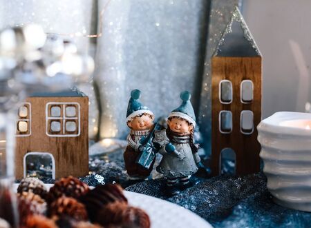 Porcelain figurines of children in a Christmas decor. Winter figurines of a boy and a girl with gifts on the background of houses and cones. Christmas Greeting card.の写真素材