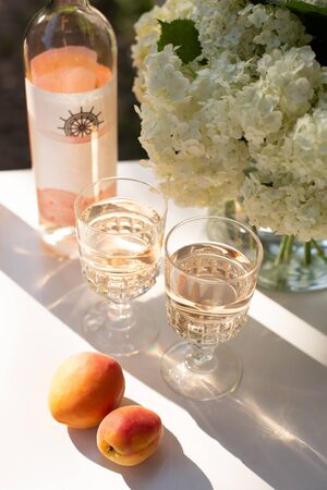 Rose wine in glasses. Rose wine on golden bottles background with flowers and fruitsの写真素材