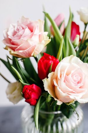 Spring bouquet in transparent glass vase. Roses, tulips and lisianthus
