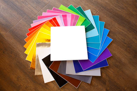 Twisted pile of colorful 12x12 sheets of adhesive paper with box isolated over the brown background....