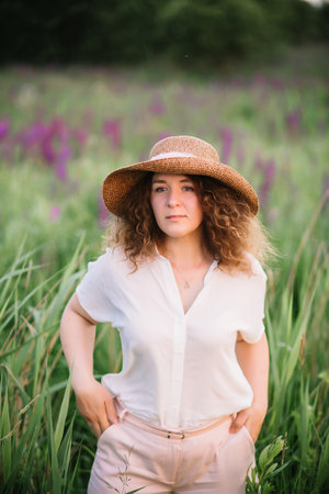 Young woman stands in white shirt in field of purple and pink lupins. Beautiful young woman with...