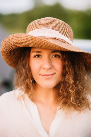 Beautiful young woman with curly hair with hat. Sunset or sunrise, bright evening light.の写真素材