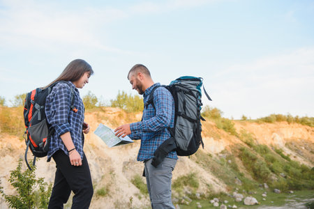 Two backpackers enjoying scenery nature view while hiking in National Park. Couple of hikers planning next way to explore holding map during travel. Infographics illustration map with top destinationsの写真素材