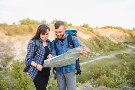 Beautiful couple of a travelers are searching way on location map while standing on high hill in sunny day, male and female hikers are walking together in mountains during long awaiting summer weekendの写真素材