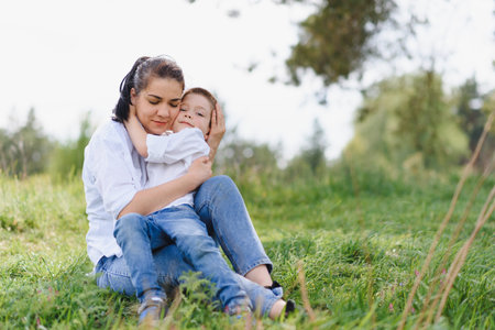 Happy young mother is playing with her baby in a park on a green lawn. Happiness and harmony of...