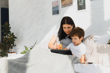 Beautiful smiling mother and son playing with digital tablet laying on bed.の写真素材