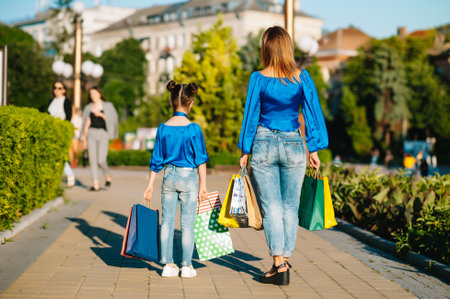 Young mother and daughter doing shopping together. woman with girl child after shopping in street. woman with daughter with shopping bags outdoors. Woman and her daughter after shopping.の写真素材