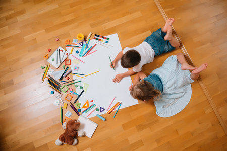 Kids drawing on floor on paper. Preschool boy and girl play on floor with educational toys - blocks,...