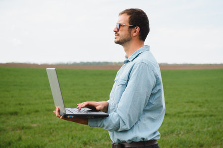 Man farmer working on a laptop in the field. Agronomist examines the green sprout winter wheat.の写真素材