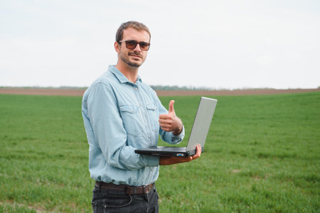 Man farmer working on a laptop in the field. Agronomist examines the green sprout winter wheat.