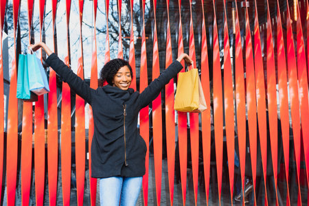 Attractive young African-American woman shopping - shopping bags, outdoors, street view, suitable for holiday shopping themes, among othersの写真素材