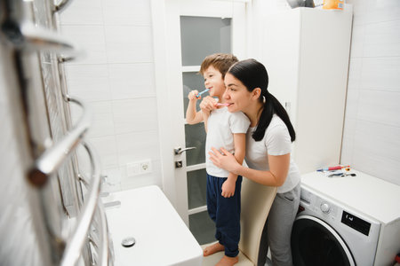 Beautiful mother and happy son brushing teeth near mirror in bathroomの写真素材