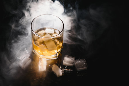 whiskey with ice on black background with smokeの写真素材