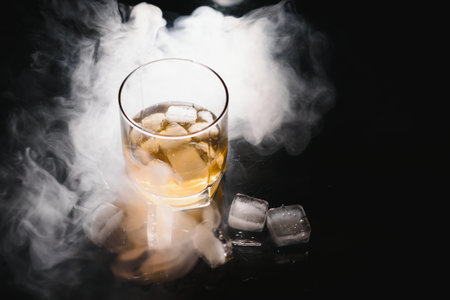whiskey with ice on black background with smokeの写真素材
