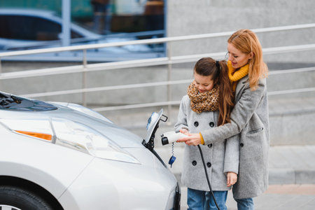 Stylish mother and daughter charge an electric car, and spend time togetherの写真素材