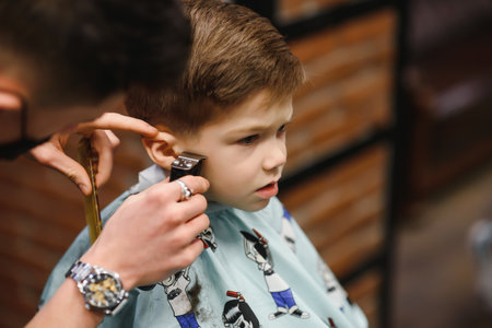 Side view of cute little boy getting haircut by hairdresser at the barbershopの写真素材