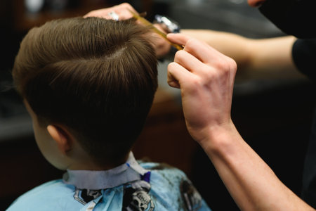 A little cute boy sits in a hairdresser's at the stylist's, a schoolchild is getting hair cut in a beauty salon, a child at a barbershop's, a short men's haircut.の写真素材